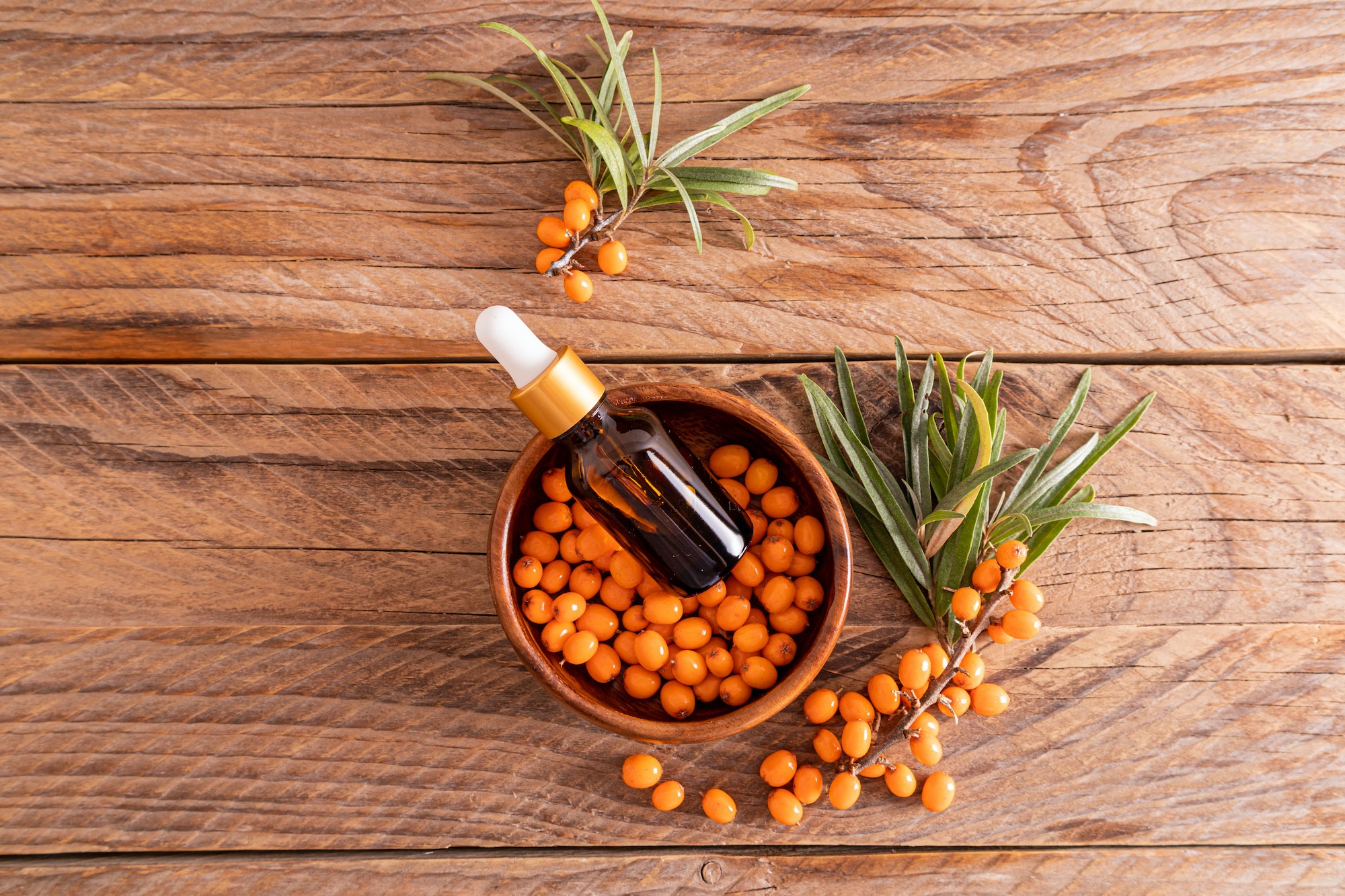 top view of a cosmetic bottle with a sea buckthorn anti-wrinkle agent in a bowl with sea buckthorn .